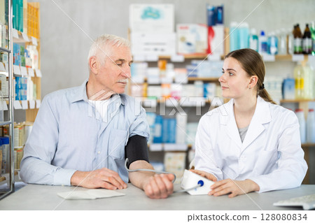 Young female pharmacist measuring blood pressure of mature man 128080834