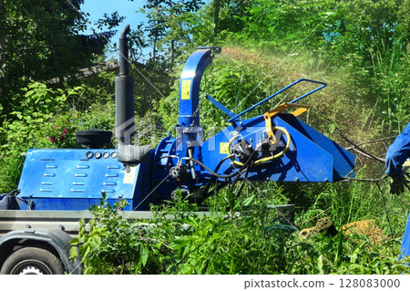 An operator loads tree branches into a wood chipper. 128083000
