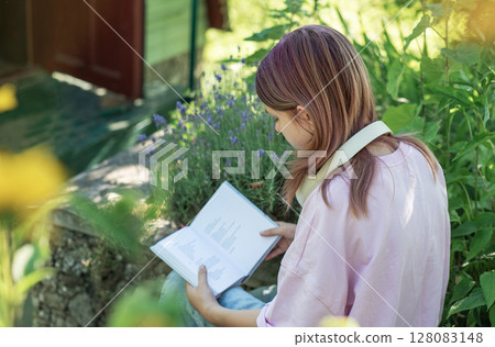 Young woman reading a book in a garden surrounded by lavender Young woman reading a book in a garden surrounded by lavender 128083148