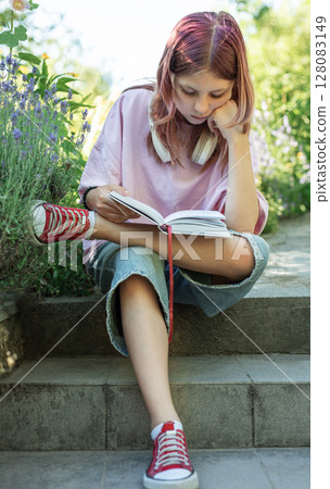 Teenage student reading a book outdoors in a garden 128083149