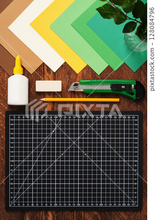 Workspace for paper crafts. Black cutting mat, colored paper, pencils, scissors, ruler, glue. Space for your text. 128084796