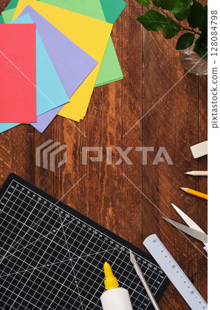 Workspace for paper crafts. Black cutting mat, colored paper, pencils, scissors, ruler, glue. Space for your text. 128084798