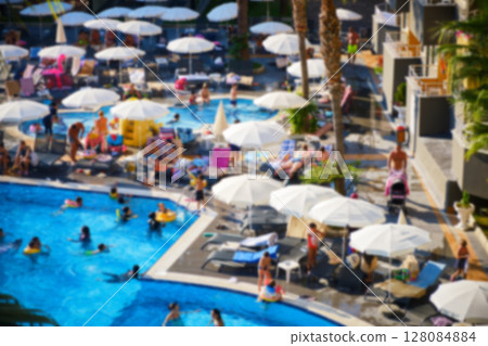 Crowded resort swimming pool with umbrellas and sunbeds 128084884