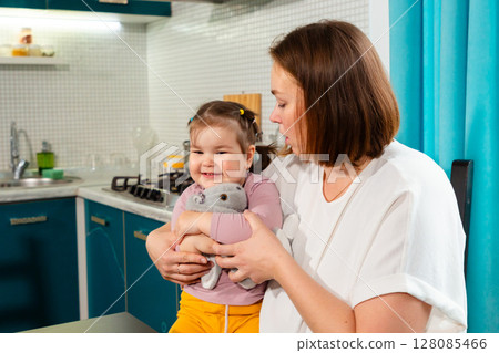 Curious smiling child learning through game with loving woman in kitchen. Concept of nurturing growth and emotional connection 128085466