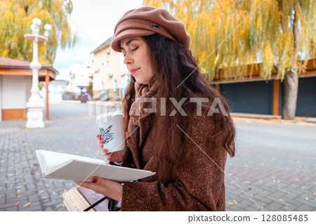 Young beautiful Caucasian woman in a beige coat and beret enjoys a quiet moment reading a book on a bench in the city. Relaxed weekend, leisure reading, student lifestyle. Young beautiful Caucasian woman in a beige coat and beret enjoys a quiet moment reading a book on a bench in the city. Relaxed weekend, leisure reading, student lifestyle. 128085485
