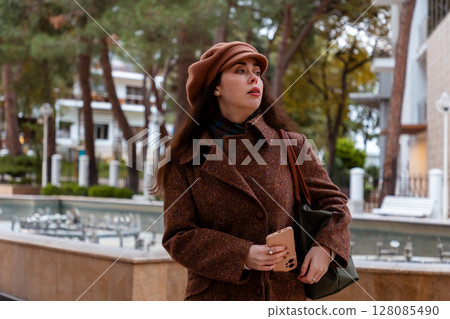 Young woman in fall fashion stays connected while walking through peaceful city streets on a bright and colorful weekend. 128085490