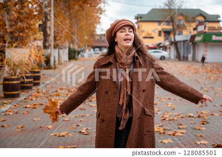Happy young lady in an elegant coat walks through the city during autumn, taking in the seasonal beauty, the golden trees, and the relaxing rhythm of a weekend. Happy young lady in an elegant coat walks through the city during autumn, taking in the seasonal beauty, the golden trees, and the relaxing rhythm of a weekend. 128085501