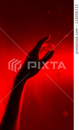 A Haunting Glimpse Beneath the Surface: A Hand Reaches Out Against a Vivid Red Background Captured in the Deep Waters of a Mysterious Scene 128086115