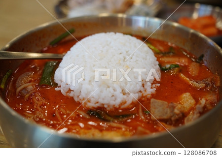 Close-up of Korean Spicy Pork Soup with a Whole Bowl of Steamed White Rice Flipped Onto the Top in a Brass Bowl 128086708