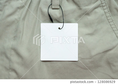 Blank white clothes tag label on gray fabric texture background Blank white clothes tag label on gray fabric texture background 128086929