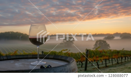 Red wine glass on mist covered wooden barrel with vineyard landscape in the blurry background Red wine glass on mist covered wooden barrel with vineyard landscape in the blurry background 128088077