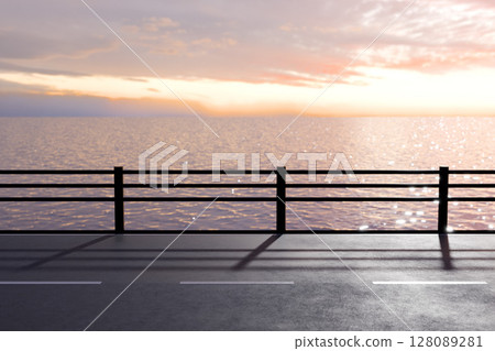 A road along the sea with a guardrail where the setting sun reflects off the sparkling sea surface 128089281