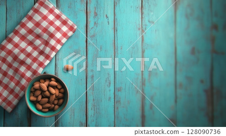 Bowl filled with almonds sits on a vibrant turquoise wooden table alongside a red and white checkered napkin, creating a cozy atmosphere 128090736