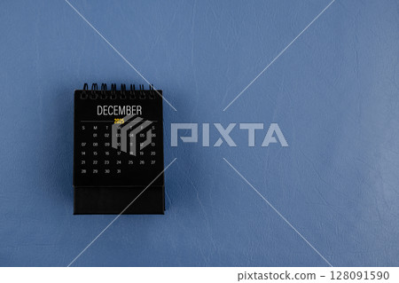 December 2025 black desk calendar on navy blue color leather background. 128091590