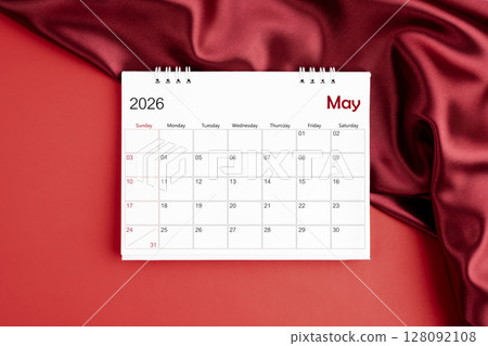 Top view of May 2026 desk calendar on red silk color background. 128092108