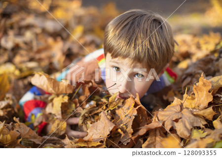 Happy little boy in a pile of yellow leaves in the autumn park. 128093355