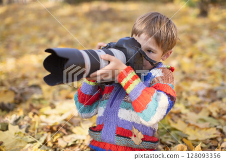 A little boy is holding a camera with a large lens. Young photographer. A little boy is holding a camera with a large lens. Young photographer. 128093356