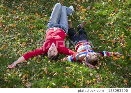 Mom and little one lie on the grass in the autumn park. Mom and little one lie on the grass in the autumn park. 128093396