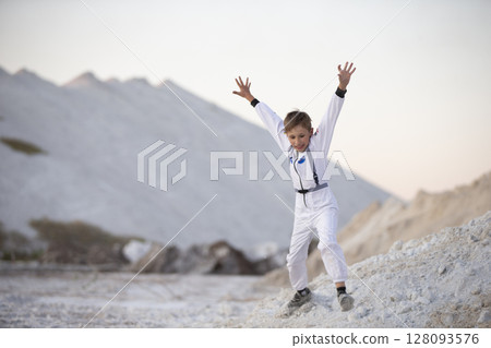 Young boy in a suit of an American astronaut jumps against a background of white mountains. Young boy in a suit of an American astronaut jumps against a background of white mountains. 128093576
