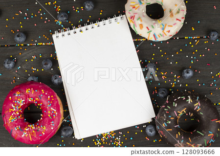 On a wooden background, blank notepad, colorful donuts and blueberries. Creative cuisine. 128093666