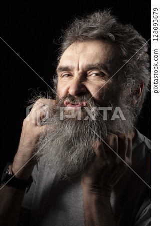 An elderly man tugs at his gray beard. An elderly man tugs at his gray beard. 128093679
