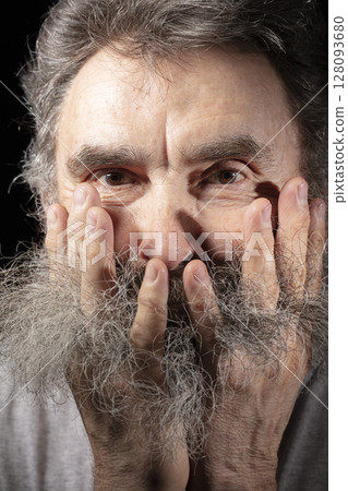 An elderly man tugs at his gray beard. An elderly man tugs at his gray beard. 128093680