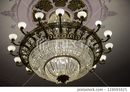 There is a beautiful theater chandelier on the ceiling and an expensive glass lamp. 128093825