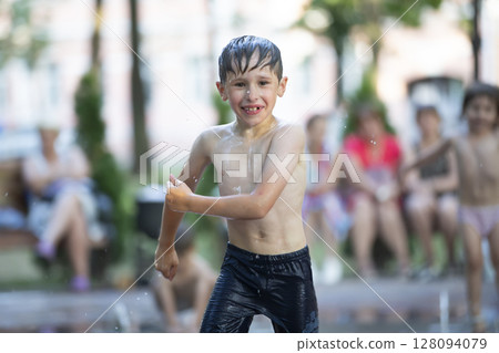 A little boy enjoys the cold waters of a fountain during the heat wave. A little boy enjoys the cold waters of a fountain during the heat wave. 128094079