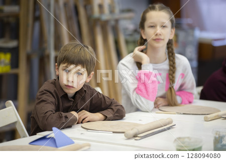 A girl and a boy are sitting at a desk in a clay modeling lesson. A girl and a boy are sitting at a desk in a clay modeling lesson. 128094080