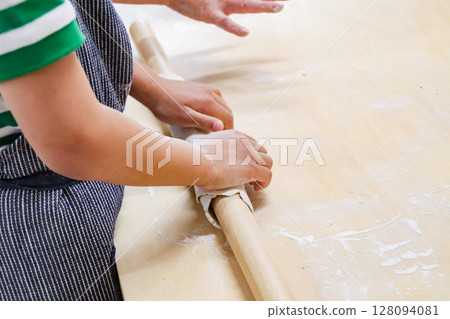 Child rolling out buckwheat dough with a rolling pin (7-year-old boy) 128094081
