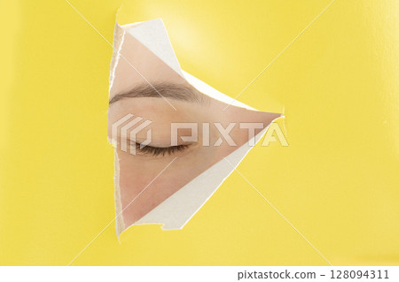 In Yellow paper with a cut out triangle in the middle, a human closed eye. 128094311