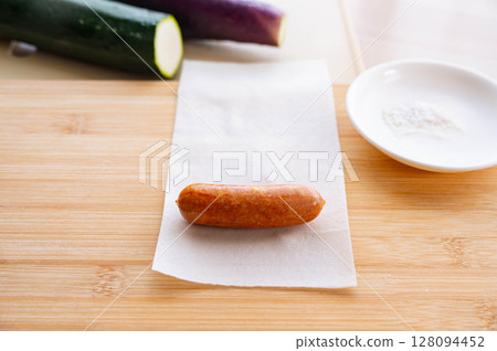 Wrap the sausage in a halved spring roll wrapper. 128094452