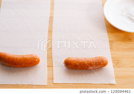 Wrap the sausage in a halved spring roll wrapper. 128094461