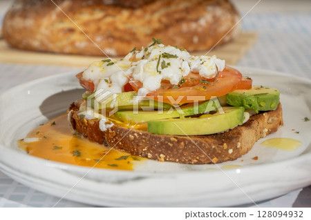 Delicious poached egg avocado toast with sliced tomatoes and herbs Delicious poached egg avocado toast with sliced tomatoes and herbs 128094932