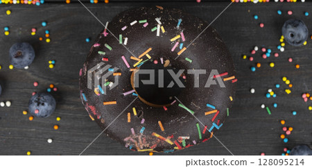 Beautiful sweet food. Colorful chocolate donut with colored sprinkles on a wooden background. 128095214