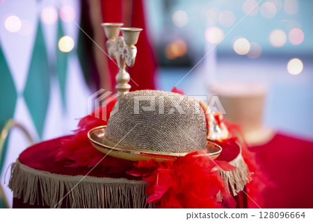 On the velvet tablecloth lies a golden theatrical hat with feathers and a candlestick. 128096664