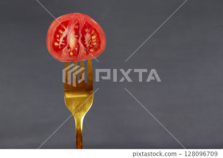 On a gold fork, a red tomato on a gray background. Creative food or vegetables.Healthy food concept. 128096709