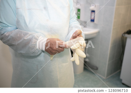 The doctor puts rubber gloves on his hands. 128096710