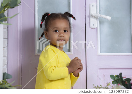 A little funny African American girl stands near a closed door. A little funny African American girl stands near a closed door. 128097282