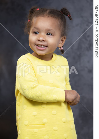 A little African American girl in a yellow dress smiles. A little African American girl in a yellow dress smiles. 128097286