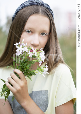 A teenage girl with creative makeup holds a bunch of wildflowers in her hands. Cute girl with long hair in the meadow.Pretty smiling girl relaxing outdoor A teenage girl with creative makeup holds a bunch of wildflowers in her hands. Cute girl with long hair in the meadow.Pretty smiling girl relaxing outdoor 128097831