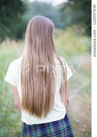 A girl with long white hair from behind against a background of a green meadow. 128097836