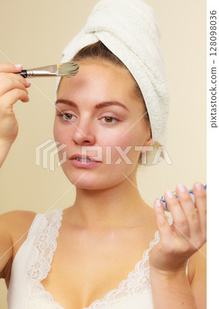 Woman applying with brush clay mud mask to her face 128098036