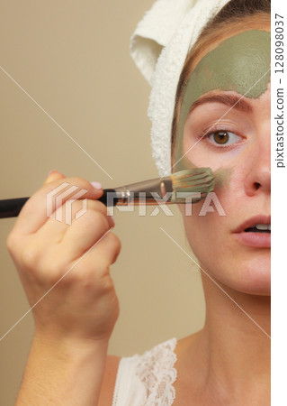 Woman applying with brush clay mud mask to her face Woman applying with brush clay mud mask to her face 128098037