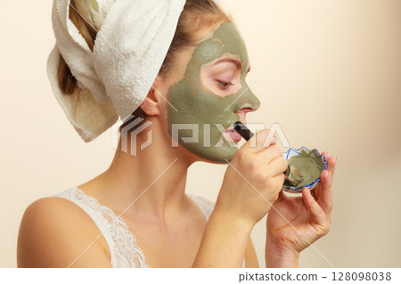 Woman applying with brush clay mud mask to her face Woman applying with brush clay mud mask to her face 128098038