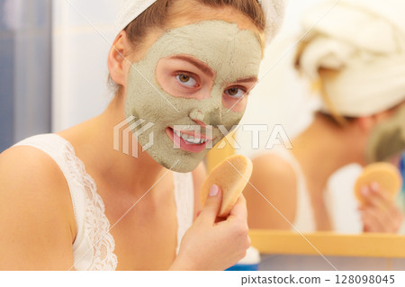 Woman removing facial clay mud mask in bathroom 128098045