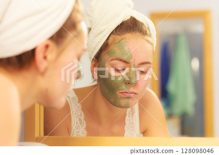 Woman removing facial clay mud mask in bathroom 128098046