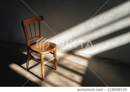 Wooden chair in sunlight casting long shadow across minimalist empty floor 128098530
