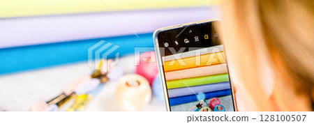 A woman takes a photo on a smartphone. Accessories for hobby embroidery knitting 128100507