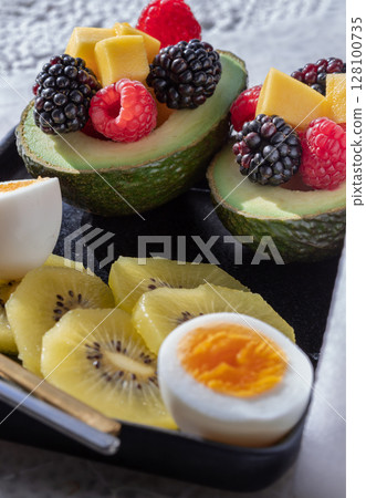 A colorful healthy food with redberry, blackberry and mango on avocado with golden kiwi and boiled egg on vibrant eating ceramic dish. 128100735